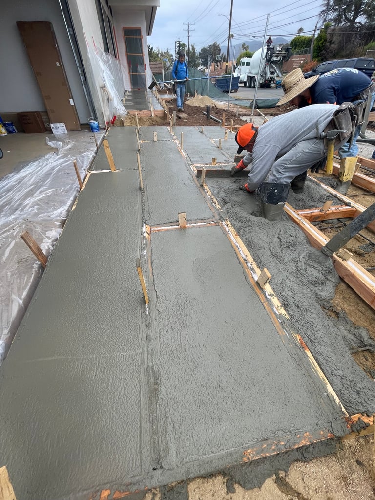 Construction worker in orange hardhat pouring and smoothing concrete on residential foundation slab using tools
