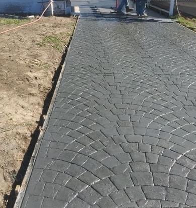 Newly installed gray paver brick driveway with herringbone pattern next to unpaved dirt area and metal edging