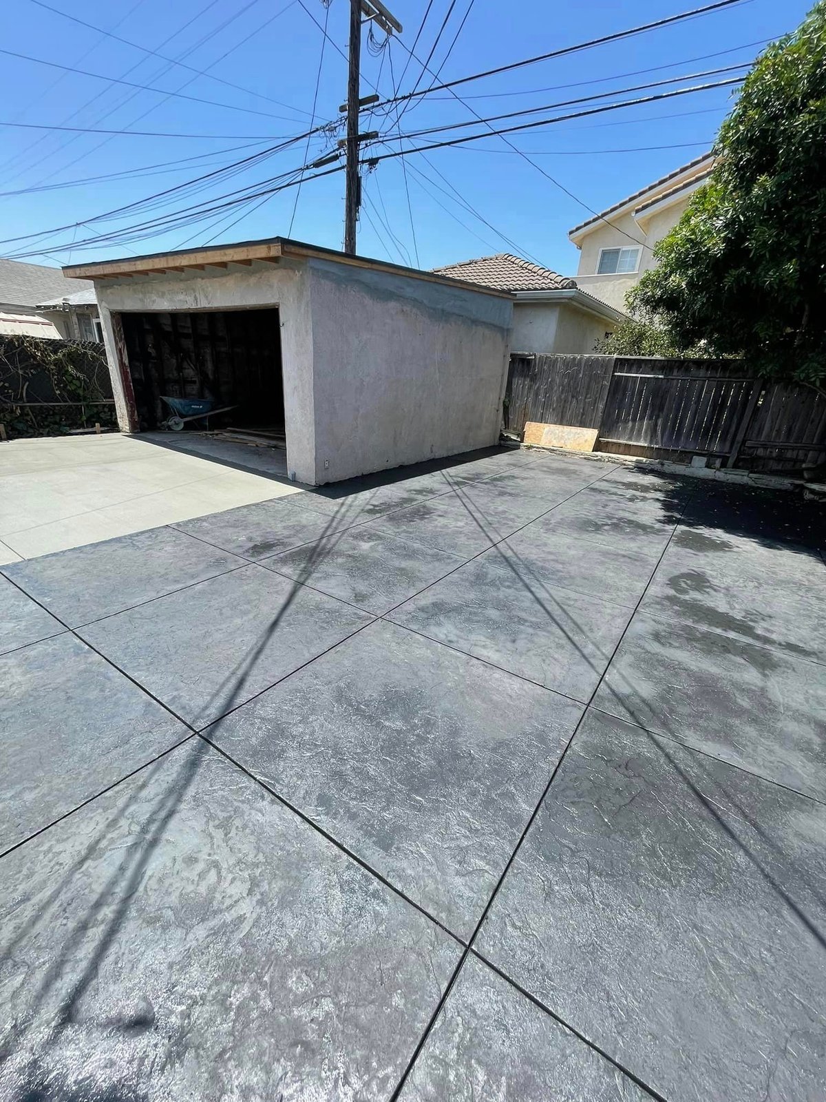 Concrete driveway with garage in residential area, power lines overhead and wooden fence visible