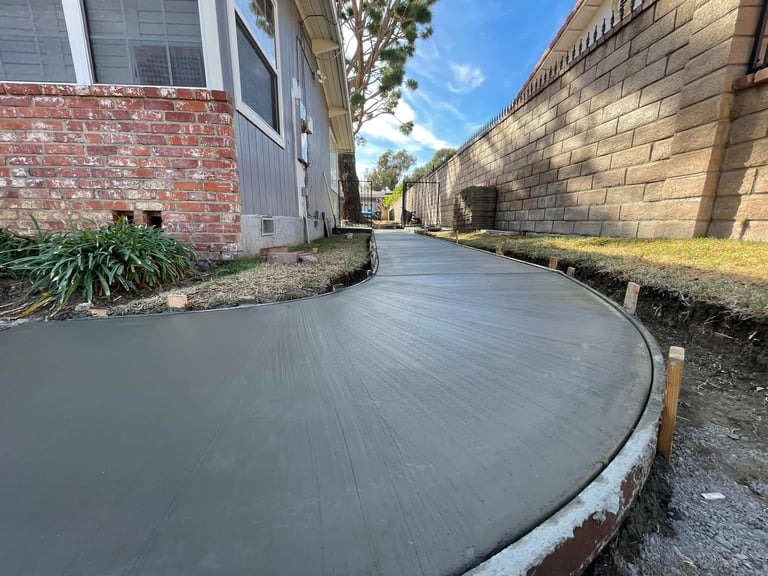 Freshly poured concrete pathway between brick buildings with landscaping on sunny day