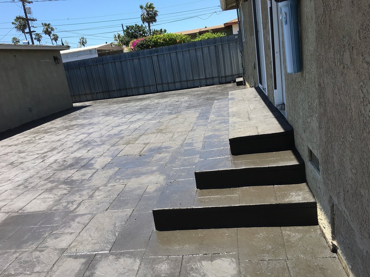 Modern rooftop patio with gray pavers, black steps, metal railing, and decorative planter box on sunny day