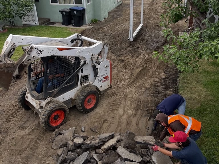 Skid steer loader and workers removing rocks and debris from residential yard during landscaping project
