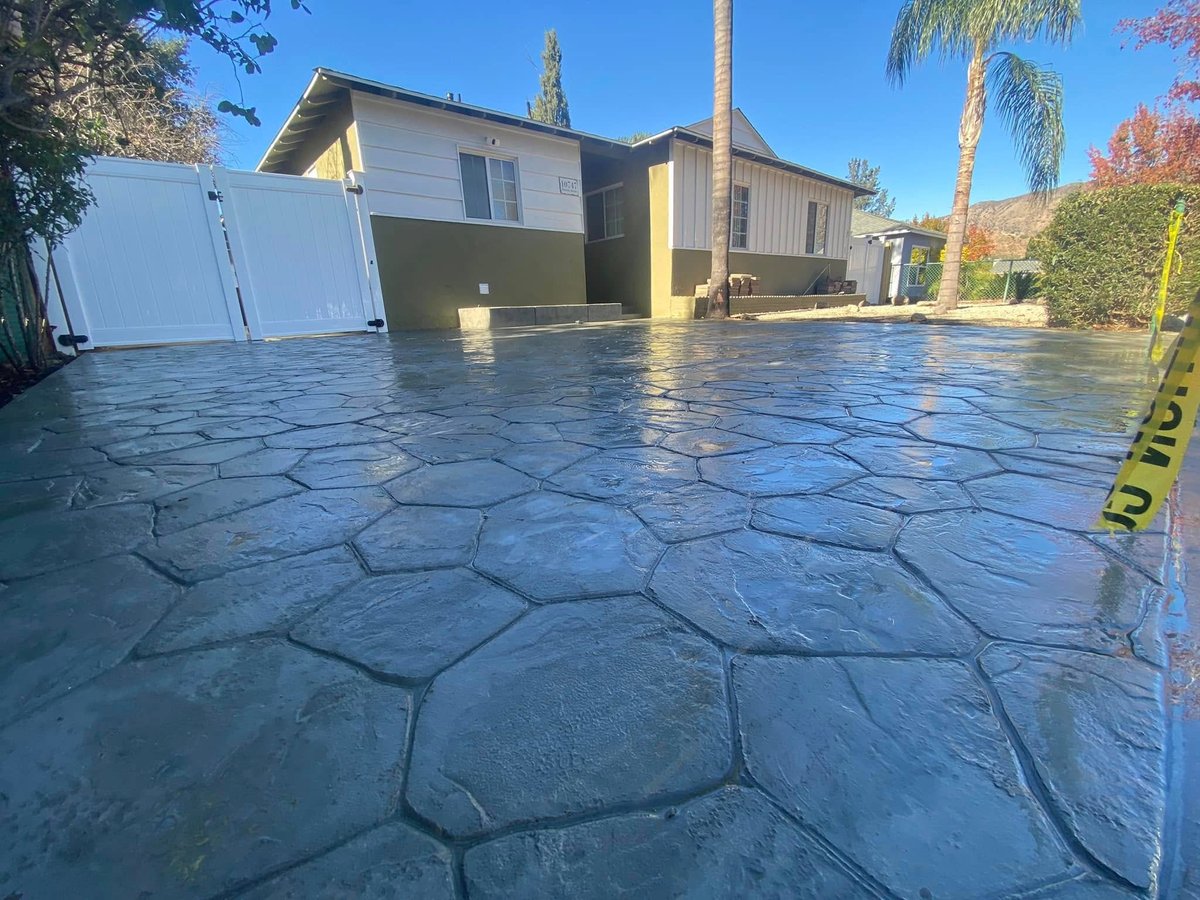 Wet stamped concrete driveway in front of modern house with trees under clear blue sky