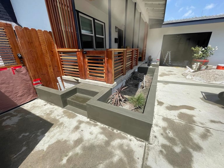 Modern backyard patio with wooden deck, raised concrete planter, and minimalist landscaping under bright sunlight